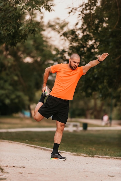 Heureux sportif positif pendant l'entraînement en plein air homme portant une tenue de sport échauffant les muscles appréciant un mode de vie actif à l'extérieur dans le parc