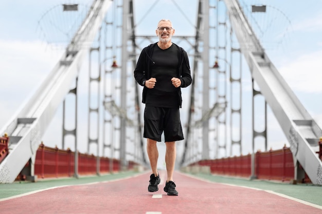Heureux sportif senior en bonne forme faisant du jogging près de l'espace de copie du pont de la ville