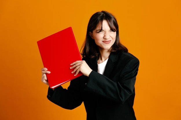 Heureux tenant dossier avec stylo jeune belle femme portant une veste noire isolée sur fond orange