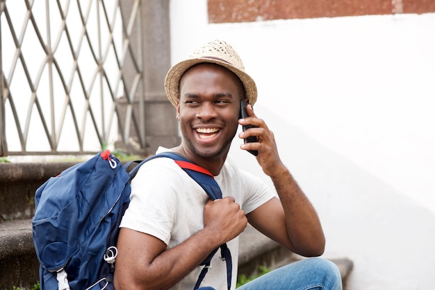 Heureux touriste afro-américain assis dans les escaliers avec sac et parler avec un téléphone portable