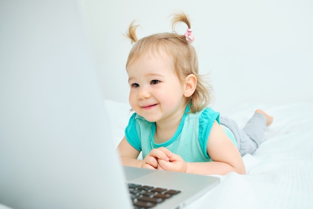 Heureux tout-petit se trouve sur le lit et regarde l'ordinateur portable