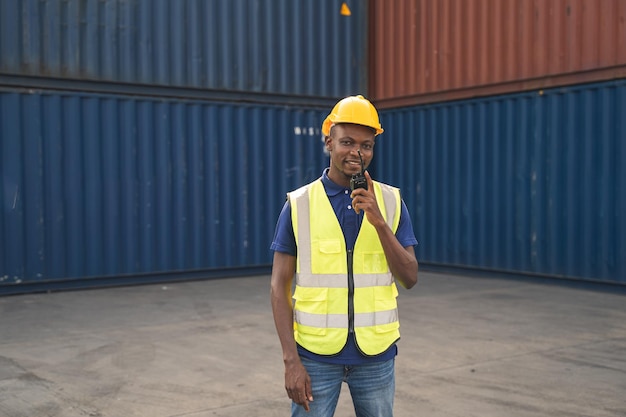 Photo heureux travailleur africain smailing debout dans le lieu de travail du conteneur et les bras croisés avec un sentiment de bonheur