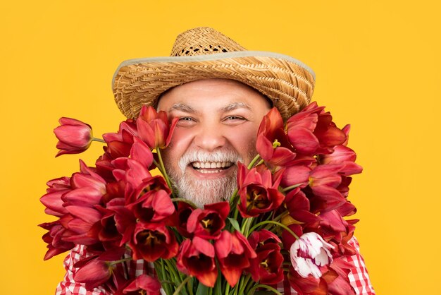 Heureux vieil homme à la retraite au chapeau tenir bouquet de fleurs de tulipe sur fond jaune