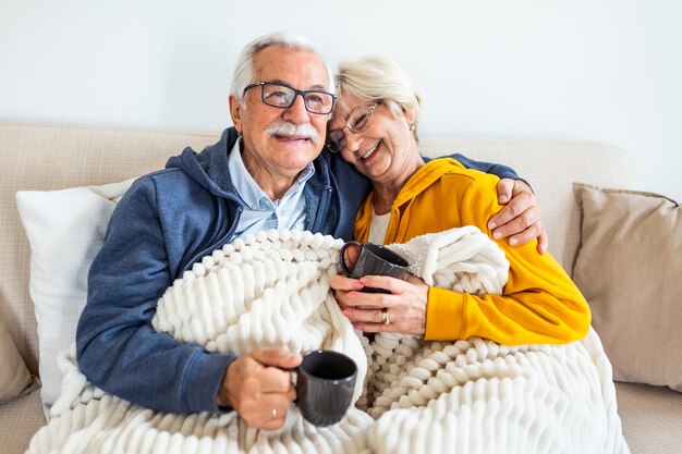 Heureux vieux couple assis sur le canapé. Se sentir bien, boire du café ou du thé