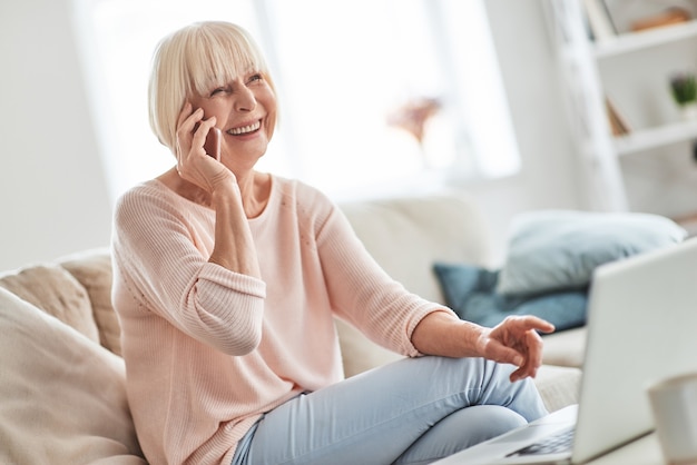 Heureux de vous entendre! Belle femme âgée parlant sur son téléphone intelligent et souriant