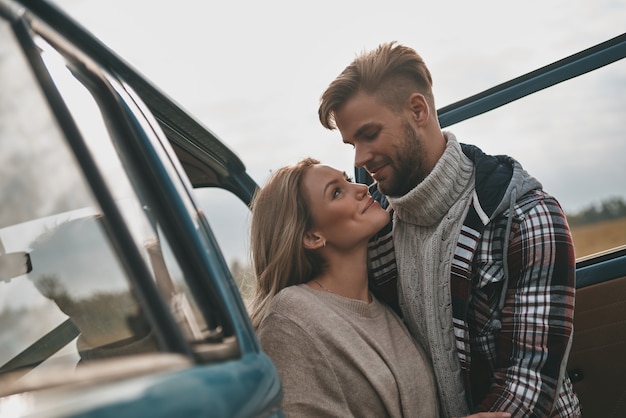 Photo heureux de voyager ensemble. beau jeune couple embrassant et souriant tout en se tenant à l'extérieur près de la mini-fourgonnette de style rétro