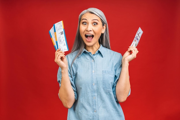 Heureux voyageur asiatique touriste âgé mature femme âgée tenant des billets et des billets d'argent isolés sur fond rouge studio Voyage de passagers à l'étranger le week-end