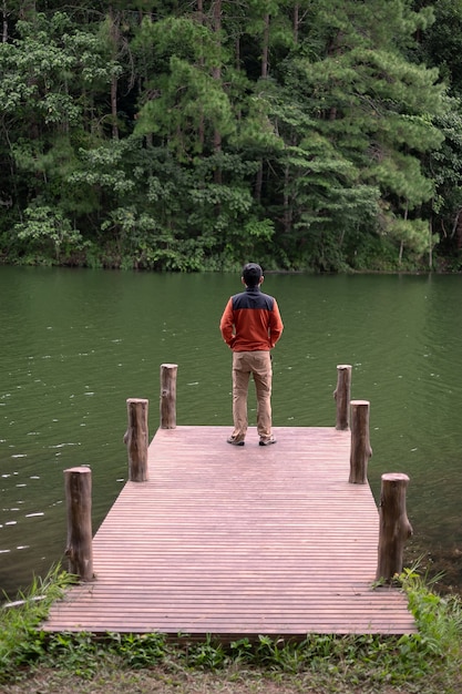 Heureux voyageur homme debout dans une jetée et regardant la rivière et le fond de la forêt