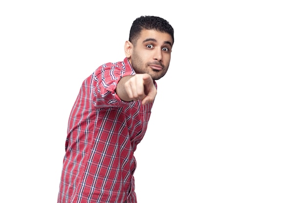 Hey vous. Portrait d'un beau jeune homme d'affaires barbu choqué en chemise à carreaux rouge debout pointant et regardant la caméra avec de grands yeux. tourné en studio intérieur, isolé sur fond blanc.