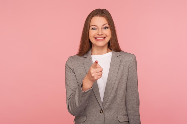 Hey vous. Portrait d'une jeune femme heureuse et optimiste en costume d'affaires faisant le choix avec le doigt indiquant, l'air ravie positive, montrant l'heureux gagnant. tourné en studio isolé sur fond rose