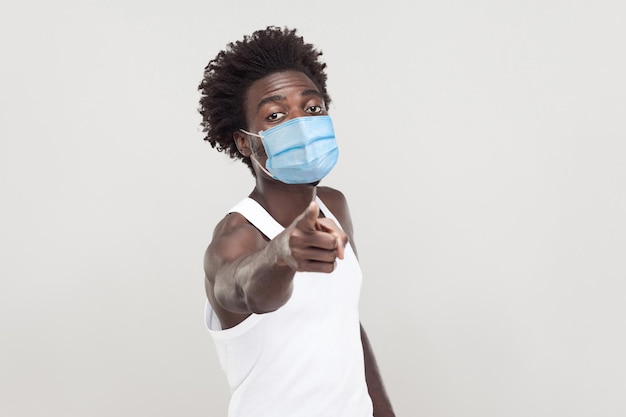 Hey vous. Portrait d'un jeune homme sérieux portant une chemise blanche avec un masque médical chirurgical debout regardant et pointant vers la caméra avec un visage sérieux. tourné en studio intérieur isolé sur fond gris.