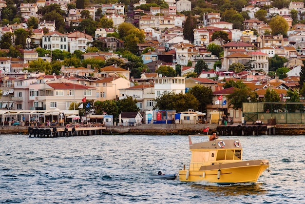 Photo heybeliada turquie 8 août 2019 bateau ou chalutier naviguant depuis la jetée de heybeliada, l'une des îles des princes dans la mer de marmara, paysage avec navire flottant jaune et façades de bâtiments insulaires depuis l'eau