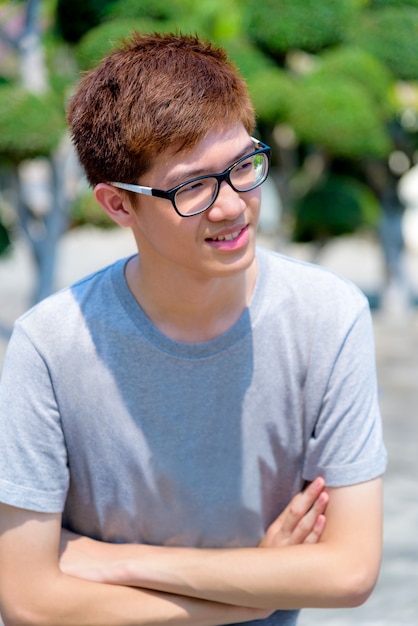 Hight angle shot Asiatique beau adolescent portant des lunettes debout les bras croisés, Portrait joyeux hipster jeune homme sourire avec un visage heureux au parc en Thaïlande