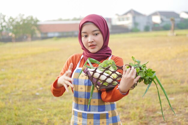 Photo hijab femme portant un tablier tenant des légumes geste pouce vers le haut