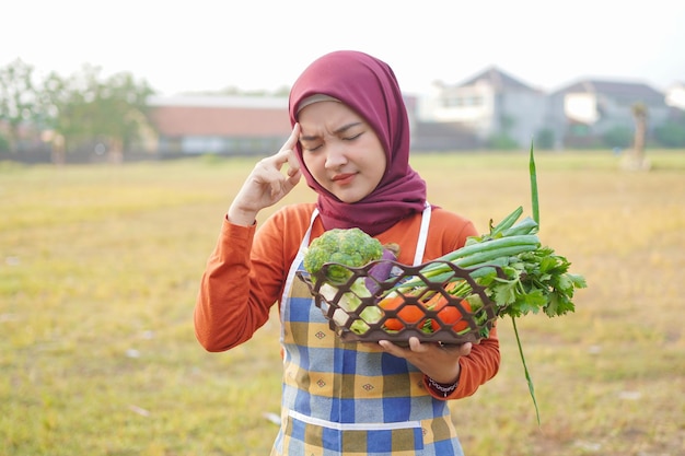 Hijab femme porter un tablier tenir des légumes et un geste de pensée