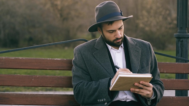 Hipser artiste créatif homme en chapeau et manteau dessin avec stylo et carnet de croquis