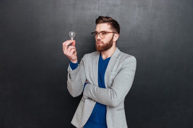 Hipster avec ampoule en studio. regardant l'ampoule. surface noire isolée