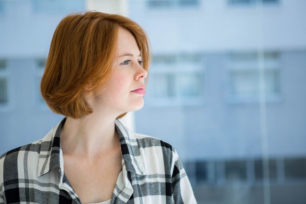 Hipster aux cheveux rouge souriant à la caméra devant une fenêtre