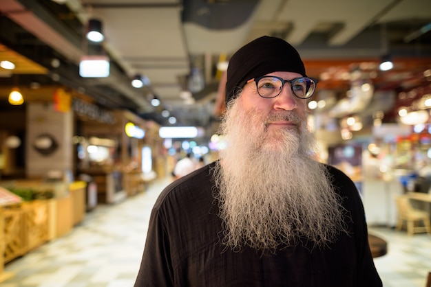 Hipster barbu mature homme avec des lunettes pensant à l'intérieur du centre commercial