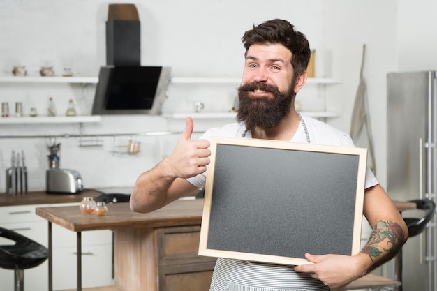 Un hipster barbu tient un tableau pour copier l'espace et affiche le menu du pouce vers le haut