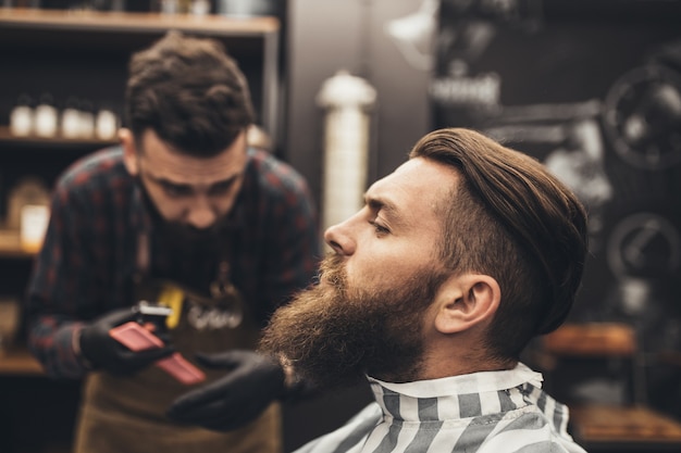 Hipster beau jeune homme visitant un salon de coiffure. Style et coupe de barbe à la mode et élégants.