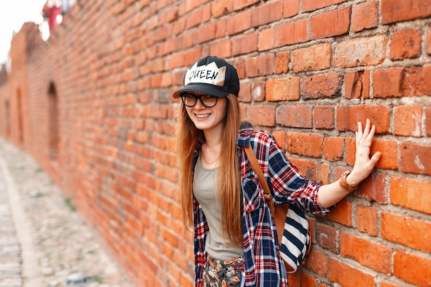 Hipster belle femme joyeuse souriant en chemise avec des lunettes près d'un mur de briques