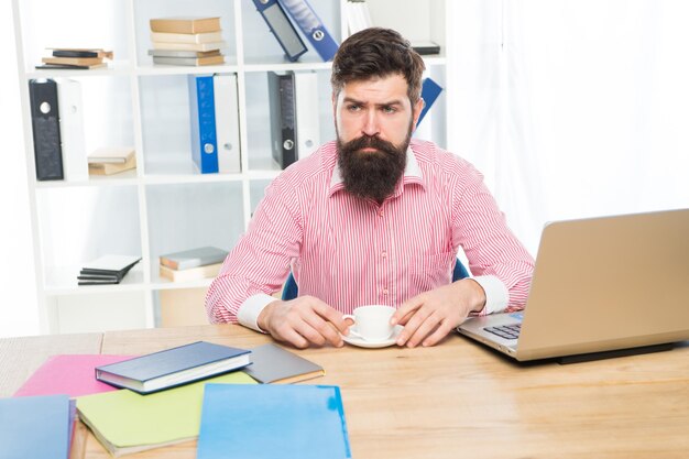 Hipster brutal avec un regard sérieux, buvez du café sur le bureau de l'agent chez un employé de bureau moderne