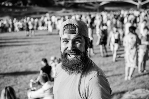 Hipster en casquette heureux de célébrer l'événement ou le festival Homme hipster barbu devant la foule Concert en plein air Fan zone Festival de musique Concept de divertissement Visitez le festival d'été Festival d'été