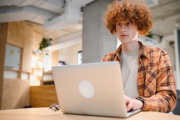 Un hipster caucasien profitant d'un travail à distance dans un café indépendant masculin dans des lunettes à la mode assis dans une cafétéria avec un ordinateur portable moderne