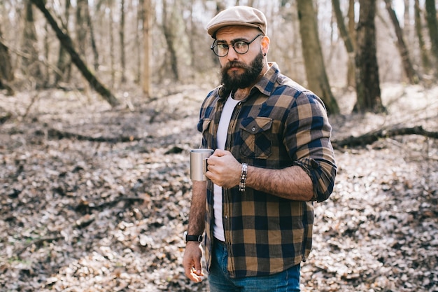 Hipster élégant avec du café dans la forêt