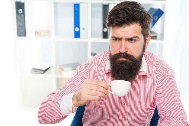 Un hipster endormi à moitié éveillé boit une tasse de café sur son lieu de travail, de la caféine.