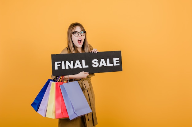 Hipster femme à lunettes et manteau avec signe de vente finale et sacs colorés isolés sur jaune