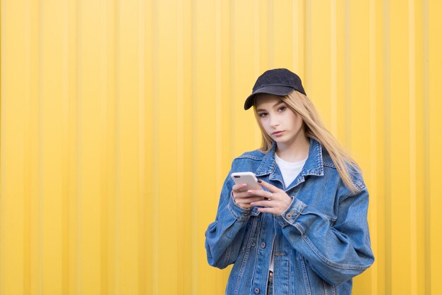 Hipster femme mignonne est sur un mur jaune avec un smartphone dans ses mains.