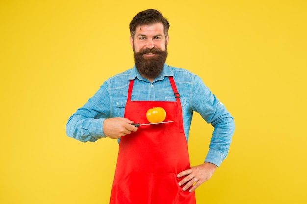 Un hipster heureux tient une tomate jaune sur un couteau pour cuisiner une perte de poids saine et délicieuse et une recette de régime