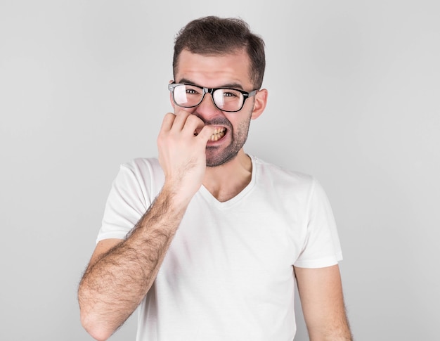 Un hipster inquiet se ronge les ongles, devient nerveux avant de passer un examen ou un événement important de sa vie. Jeune homme à la mode embarrassé peur des difficultés se dresse contre le mur gris