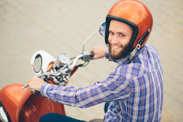 Hipster jeune homme en casque est à cheval sur un scooter rétro jaune en ville