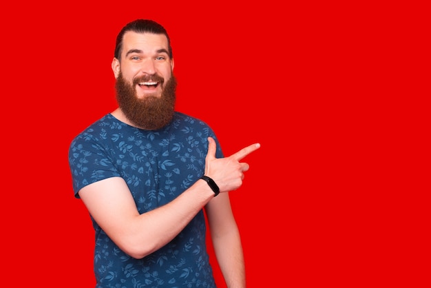 Un hipster masculin souriant pointe de côté sur le fond rouge.