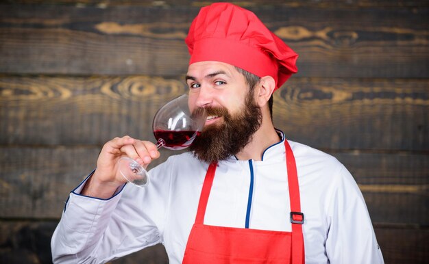 Hipster porter un chapeau et un tablier profiter de l'arôme de la boisson L'homme maître chef tient un verre de vin Quel vin servir avec le dîner Concept de dîner exquis Dégustation de vin Comment associer le vin et la nourriture comme un expert