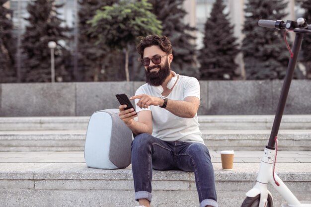 Hipster souriant à l'aide d'un smartphone dans la rue