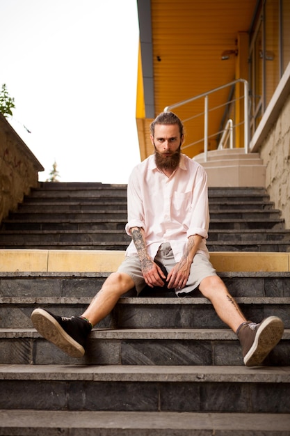 Hipster tatoué et barbu posant en plein air dans la ville