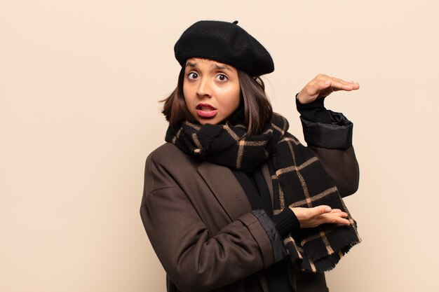 Hispanic woman holding un objet avec les deux mains sur le côté de l'espace de copie, montrant, offrant ou annonçant un objet