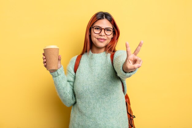 Hispanic woman smiling and looking happy gesticulant victoire ou paix étudiant avec un concept de café