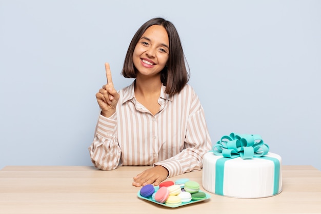 Hispanic woman smiling et à la sympathique, montrant le numéro un ou d'abord avec la main en avant, compte à rebours