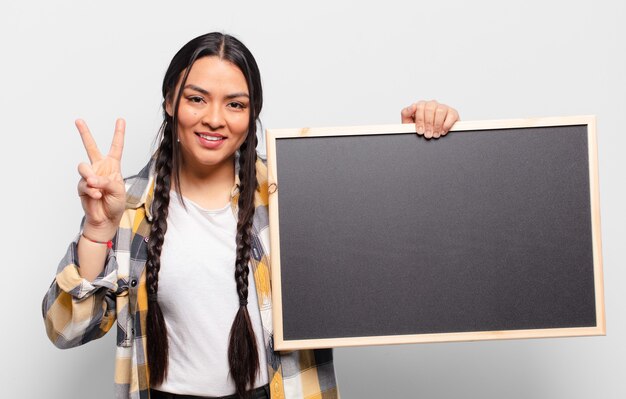 Hispanic woman smiling et à la sympathique, montrant le numéro deux ou seconde avec la main vers l'avant, compte à rebours