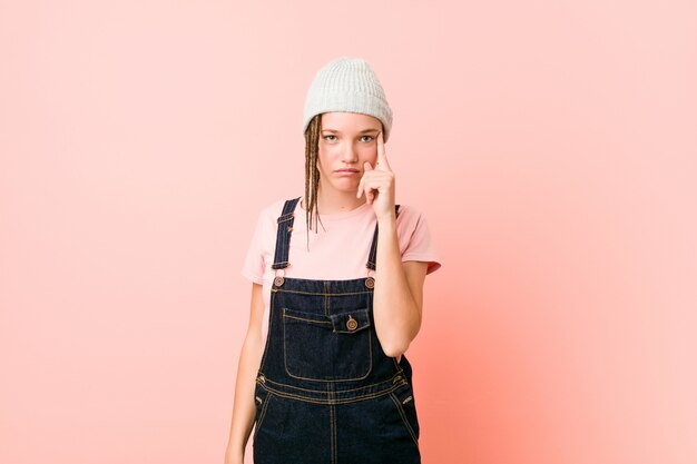 Hispter adolescent femme pointant le temple avec le doigt, pensant, concentré sur une tâche.