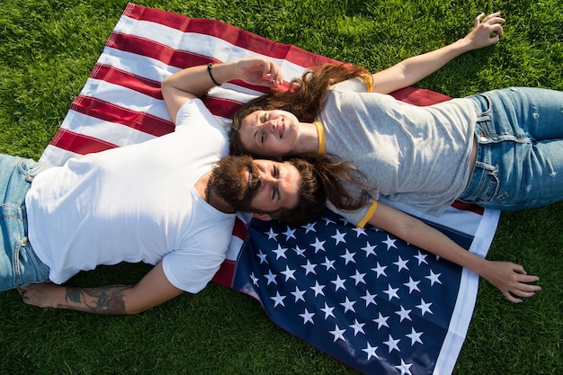 Histoire de l'Amérique. peuple patriote américain. Couple américain reposant sur le drapeau américain à l'extérieur. Le jour de l'indépendance. Fête nationale. Hipster barbu et fille amoureuse. 4 juillet. tradition américaine.