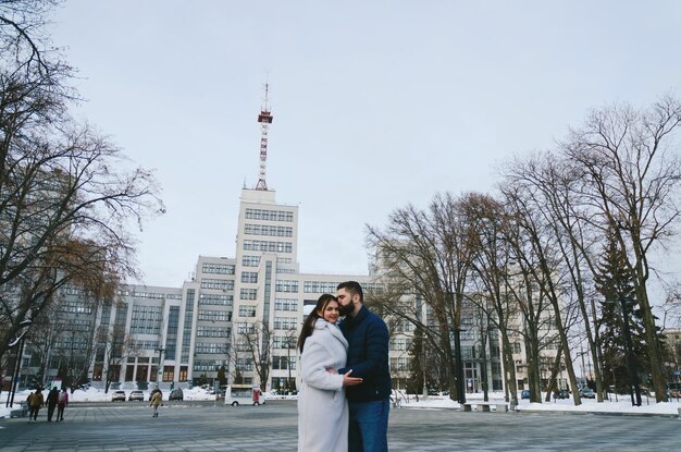 Histoire d'amour d'un couple marchant dans la ville enneigée d'hiver. Jeune homme dans une veste bleue avec barbe. jolie femme