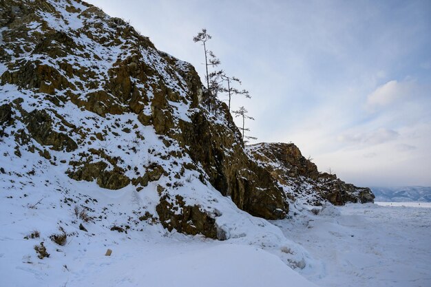 Photo hiver baïkal petite mer le royaume de la glace et de la neige lac olkhon baïkal lumière du soir à travers les arbres et les rochers