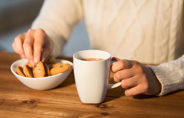 hiver, concept de nourriture et de boisson - gros plan d'une femme avec des biscuits à l'avoine et une tasse de chocolat chaud assis à une table en bois à la maison