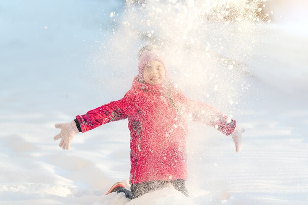 L'hiver, une fille joue dehors en jetant de la neige